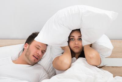 sleep apnea treatment arvada, co | woman using pillow to cover ears while man snores beside her